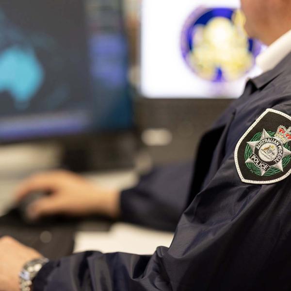 Person in police uniform working at a computer, with a focus on the police badge on their sleeve.