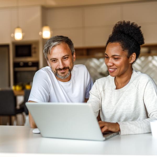 A couple sitting in their kitchen looking at a laptop screen while completing multi-factor authentication.