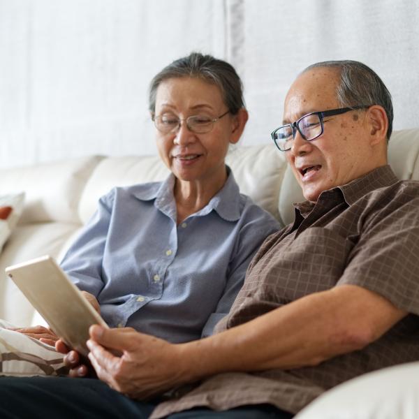 An elderly couple sitting on a coach together while installing software updates on their tablet.