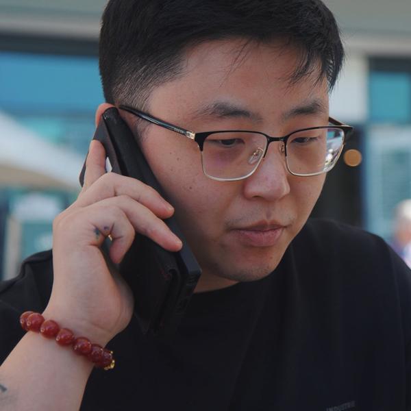 A person wearing glasses and a black shirt is holding a smartphone to their ear.